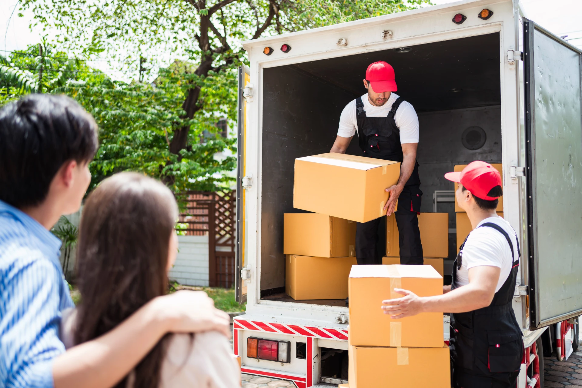 Movers loading boxes into a truck while a couple observes, showcasing a professional moving service in action. The scene emphasizes teamwork and efficiency during the relocation process.