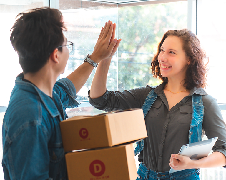 A man and a woman celebrate a successful move with a high-five while handling moving boxes in a bright, modern space. Their expressions convey teamwork and positivity.