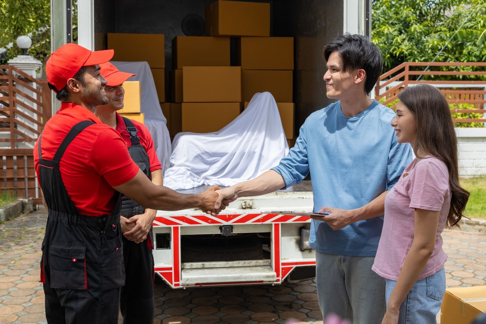 A moving service representative shakes hands with a couple in front of a moving truck filled with boxes, indicating a successful transaction. The scene conveys a sense of professionalism and customer satisfaction.