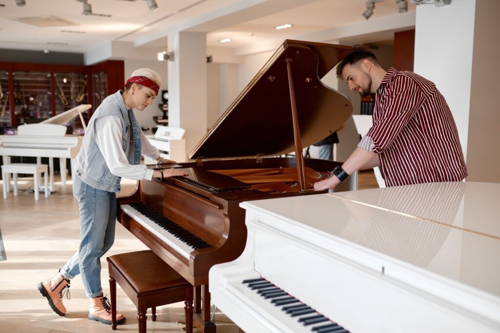 Two people examine a grand piano in a well-lit showroom filled with various pianos. The atmosphere is focused and curious, highlighting their interest.