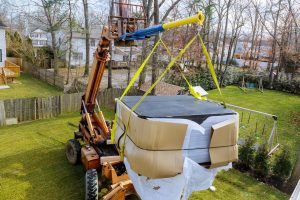 Crane lifting a hot tub over a backyard fence during a professional relocation process